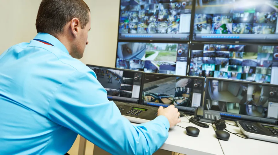 Security guard monitoring multiple surveillance camera feeds on several screens in control room