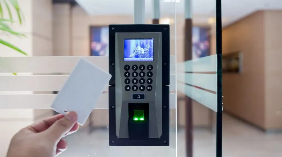 Hand holding an access card near electronic keypad and fingerprint scanner on glass door