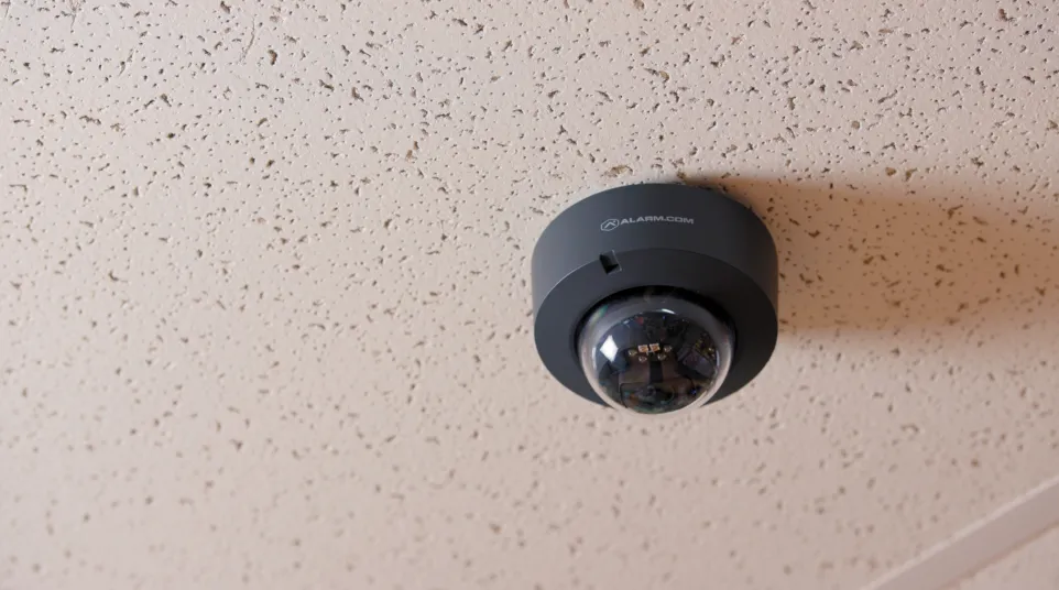 Black dome security camera mounted on textured white ceiling for indoor surveillance.