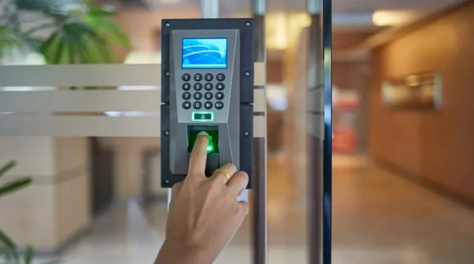 Person using fingerprint scanner and keypad on access control device at office entrance.