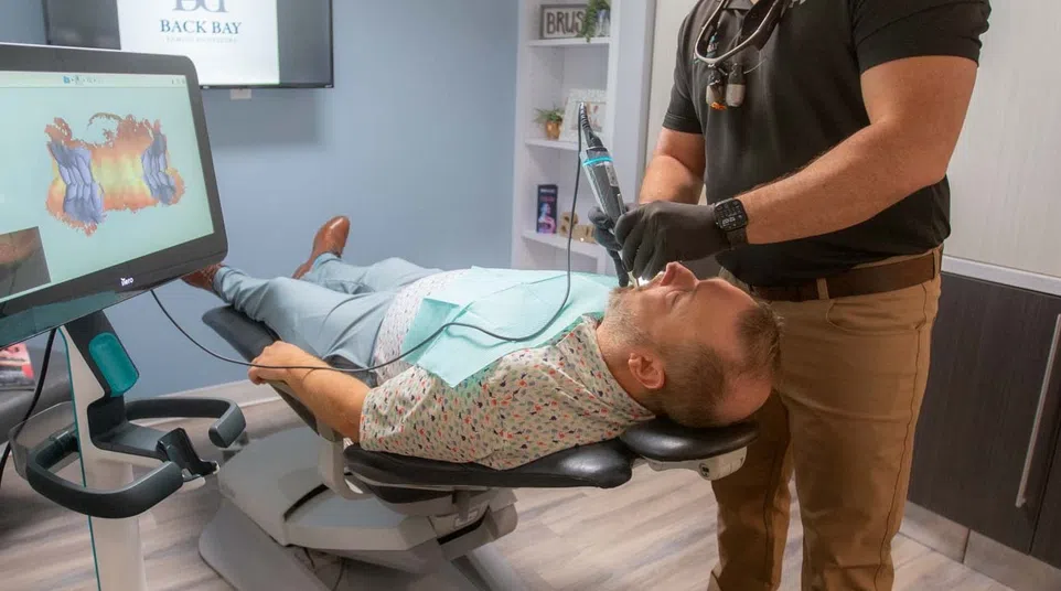 Dentist performing dental treatment on patient in modern clinic with digital imaging technology nearby