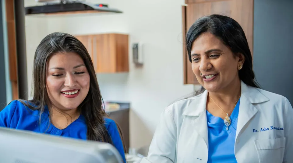 Female doctor and nurse reviewing medical information together on a computer in a clinic setting.