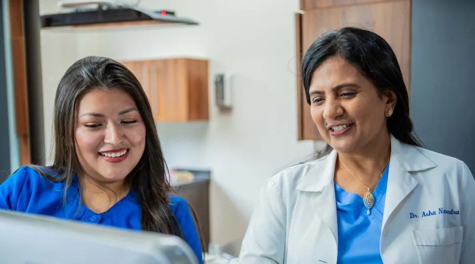 Female doctor and nurse reviewing medical information together on a computer in a clinic setting.