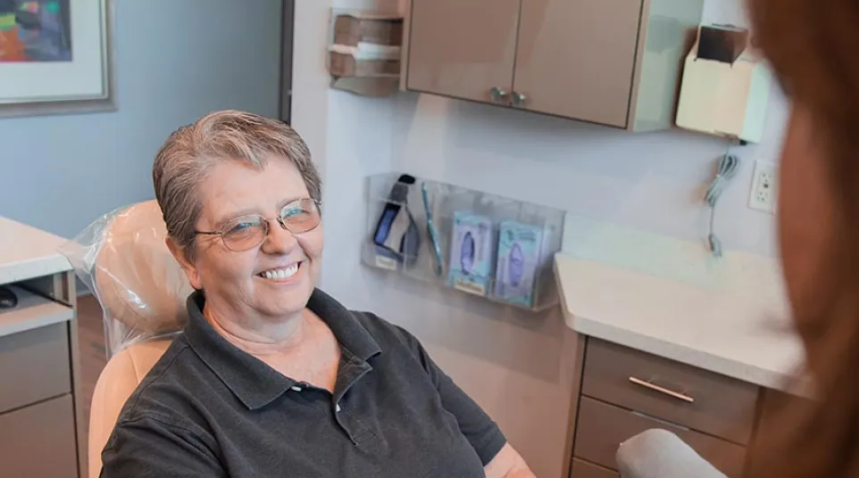 Smiling older woman sitting in dental chair during consultation at dental clinic with staff in foreground.