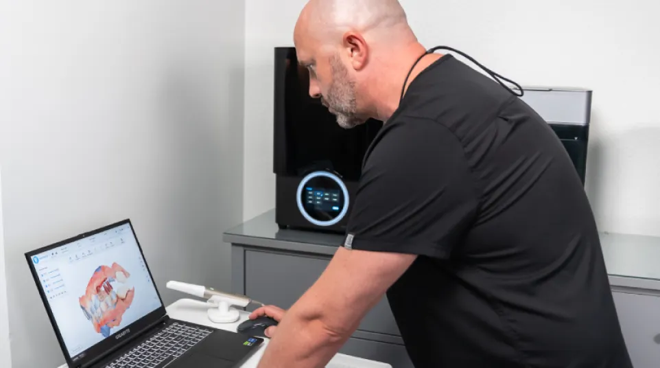Dentist reviewing 3D dental scan on laptop in modern clinic with dental equipment in background