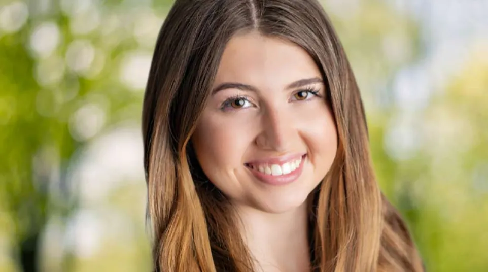 Smiling young woman with long hair outdoors, showcasing dental implant results with natural teeth and bright smile.