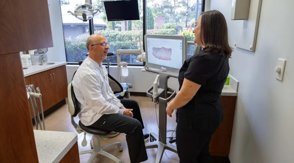 Dentist and assistant reviewing dental 3D scan images on a monitor in a modern clinic room with window views