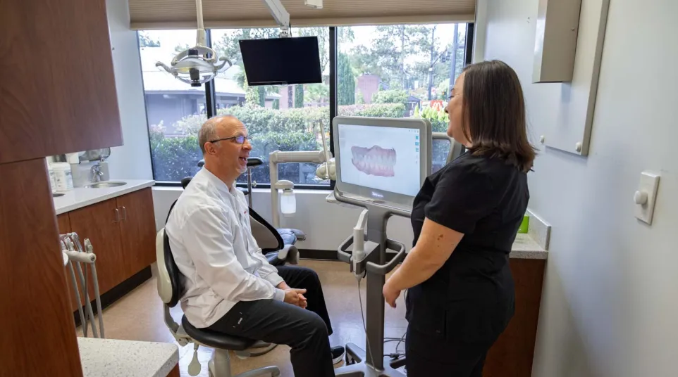 Dentist and assistant reviewing dental 3D scan images on a monitor in a modern clinic room with window views
