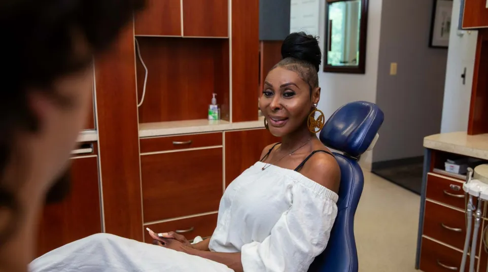 Woman in white outfit sitting in a dental chair smiling at the dentist in a clinic room