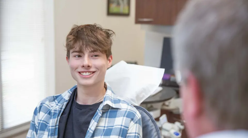 Teen boy smiling while sitting in dental chair during a checkup with dentist in clinic.