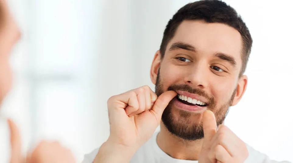 Man with beard flossing his teeth in front of a mirror for oral hygiene.