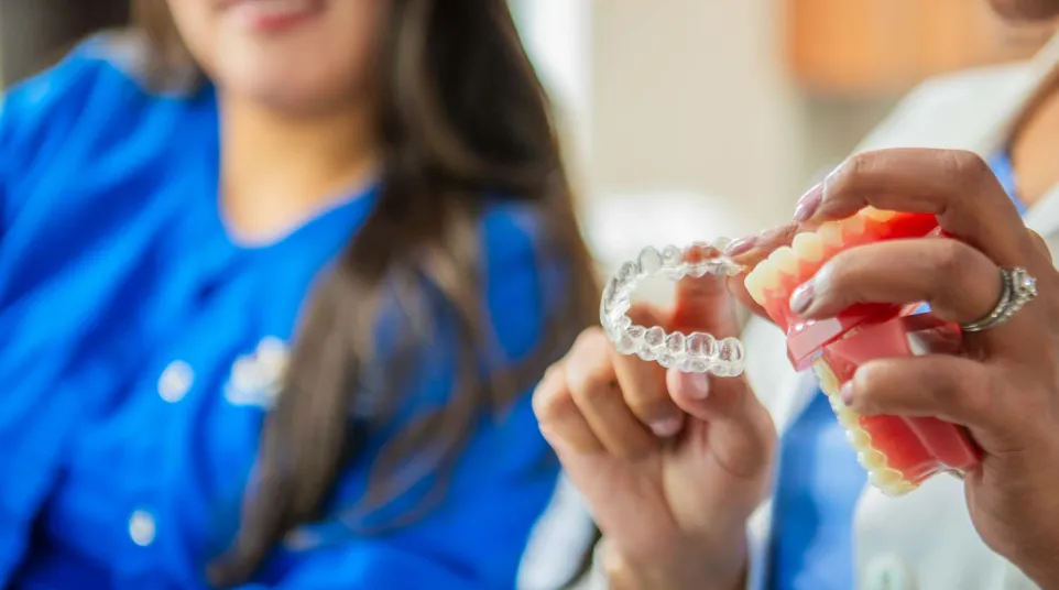 Dentist holding a dental model and clear aligner while explaining orthodontic treatment to a patient.
