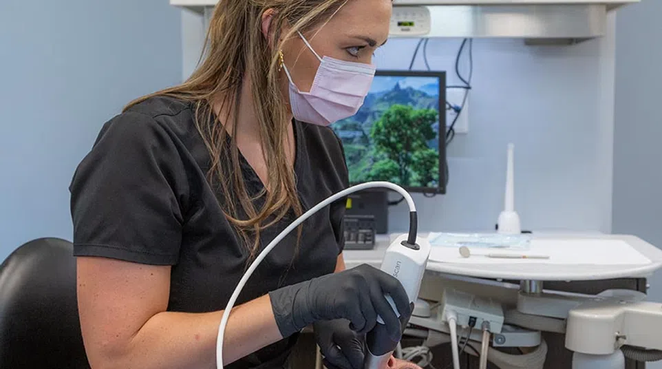 Dentist examining patient teeth with dental camera in modern clinic featuring clean blue walls and equipment.