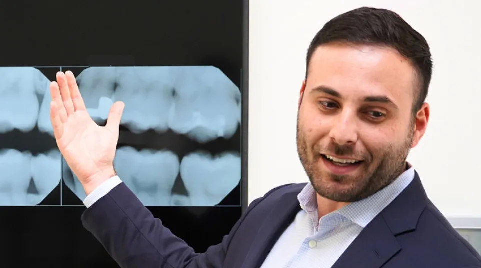 Dentist in suit explaining dental X-rays displayed on screen during consultation.