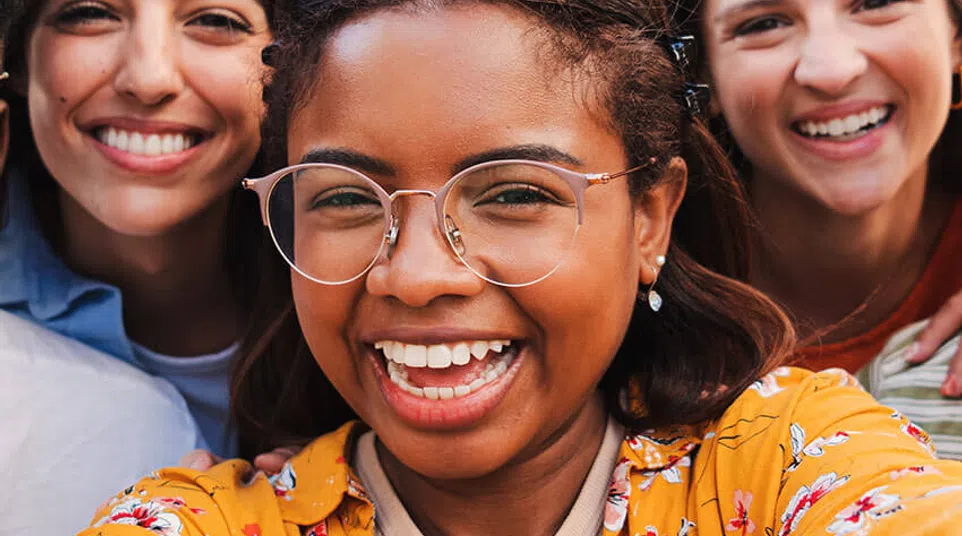 Three diverse young women smiling happily outdoors taking a close-up selfie together.