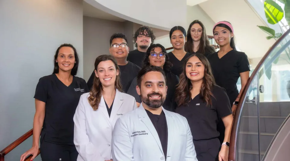Group portrait of smiling dental team members in professional attire standing on a staircase inside a clinic