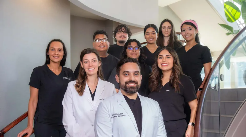Group portrait of smiling dental team members in professional attire standing on a staircase inside a clinic