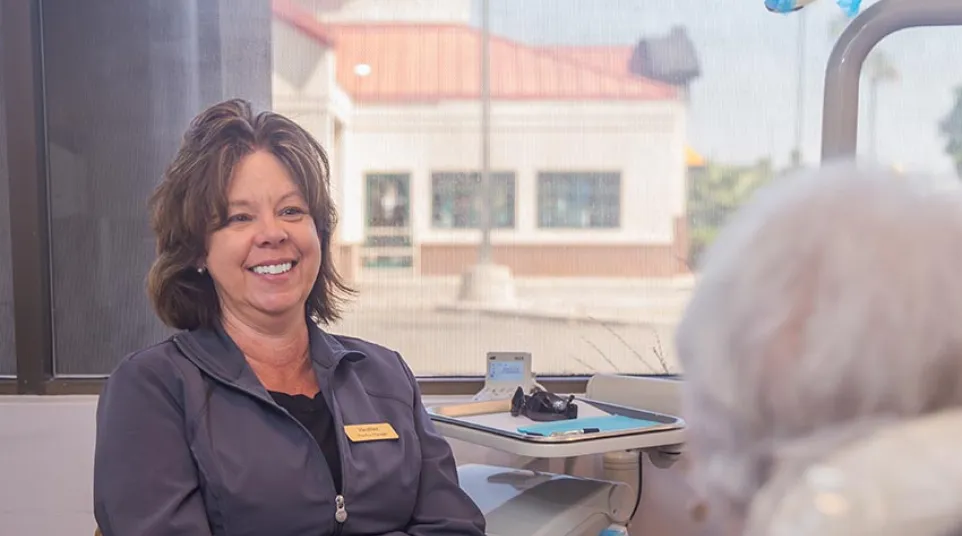 Smiling healthcare professional in uniform consulting with elderly patient in a bright clinic room.
