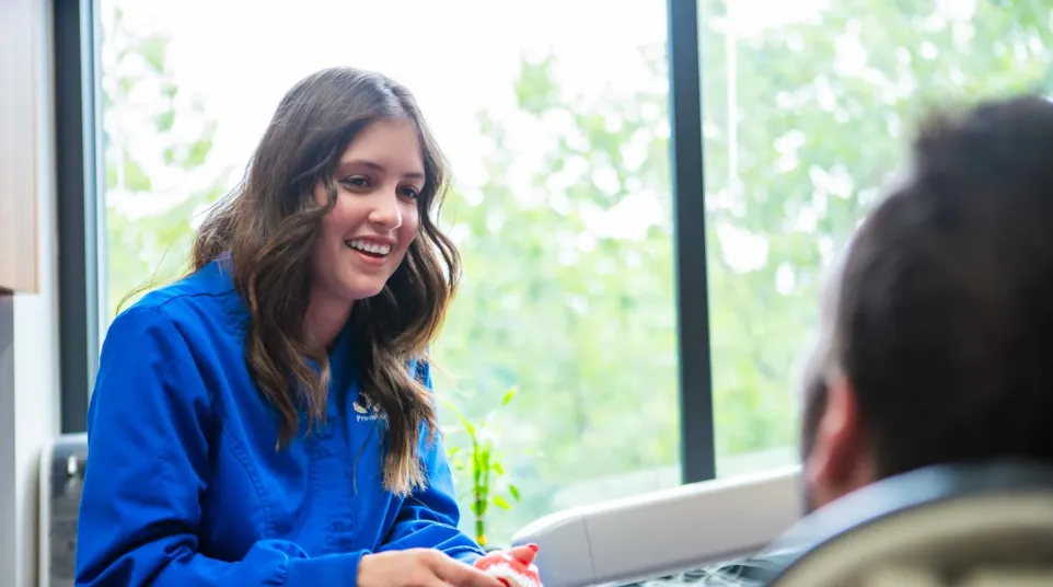 Smiling female dental professional in blue scrubs talking to patient in a bright dental office.