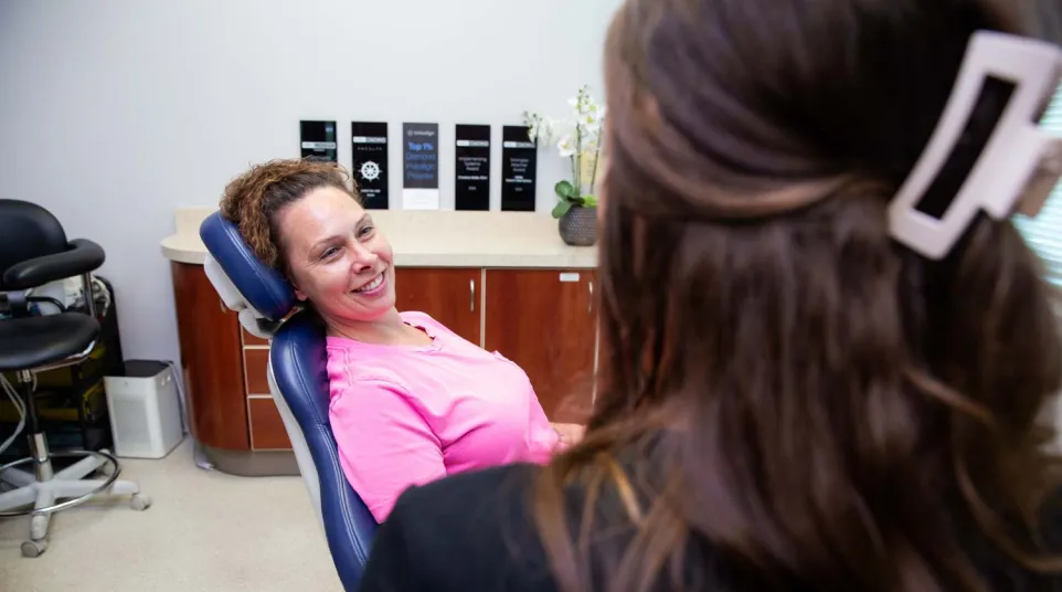 Woman in pink shirt smiling while sitting in a dental chair during a consultation with a dental professional.