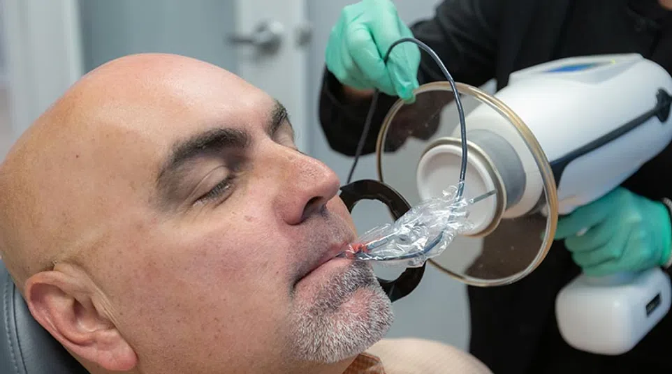 Man receiving a dental X-ray using a bitewing sensor and protective device in a dental office.
