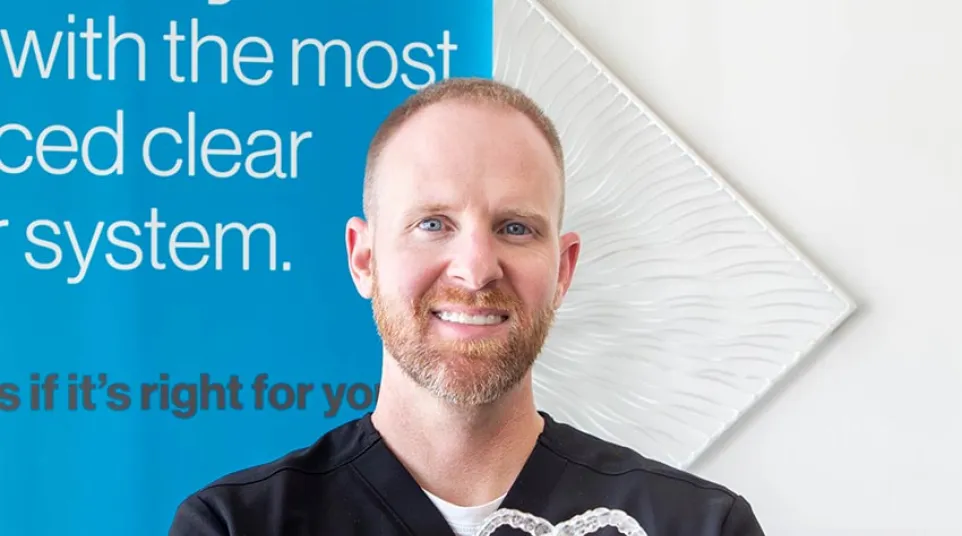 Smiling male dentist holding clear dental aligners shaped like a heart in a dental clinic.