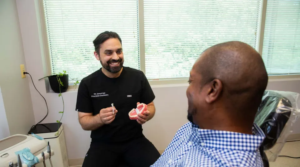 Dentist explaining dental procedure to a male patient using a teeth model in a dental clinic.
