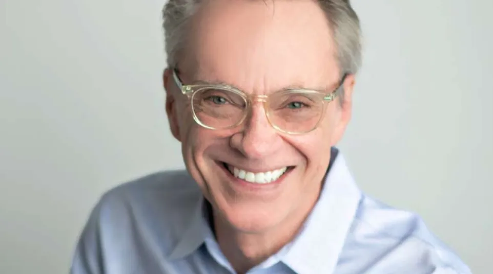 Smiling middle-aged man wearing glasses and a blue shirt showcasing bright white teeth after dental veneers and whitening.