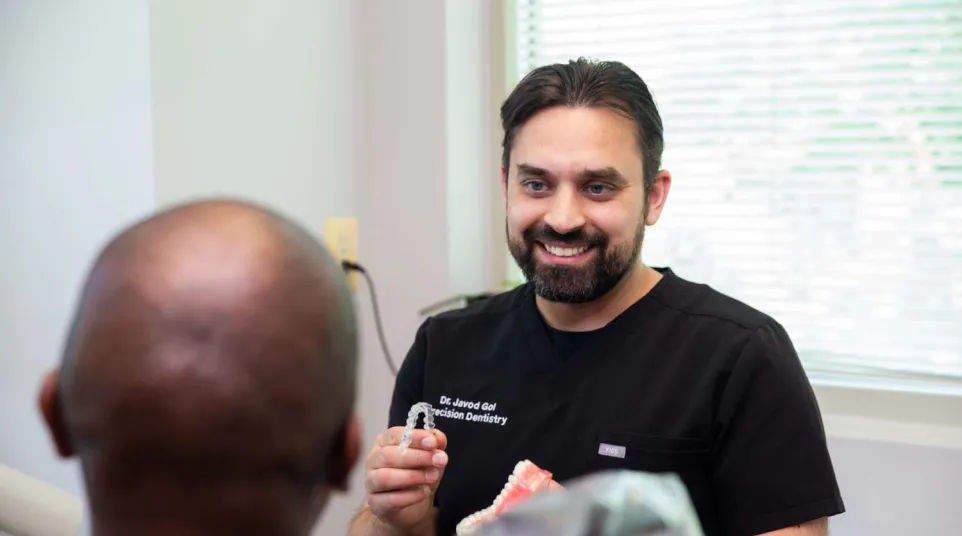 Dentist explaining dental aligners to patient in a bright dental office with smile and model teeth.