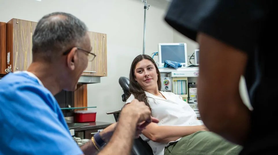 Doctor discussing treatment with a female patient seated in a medical office exam chair.