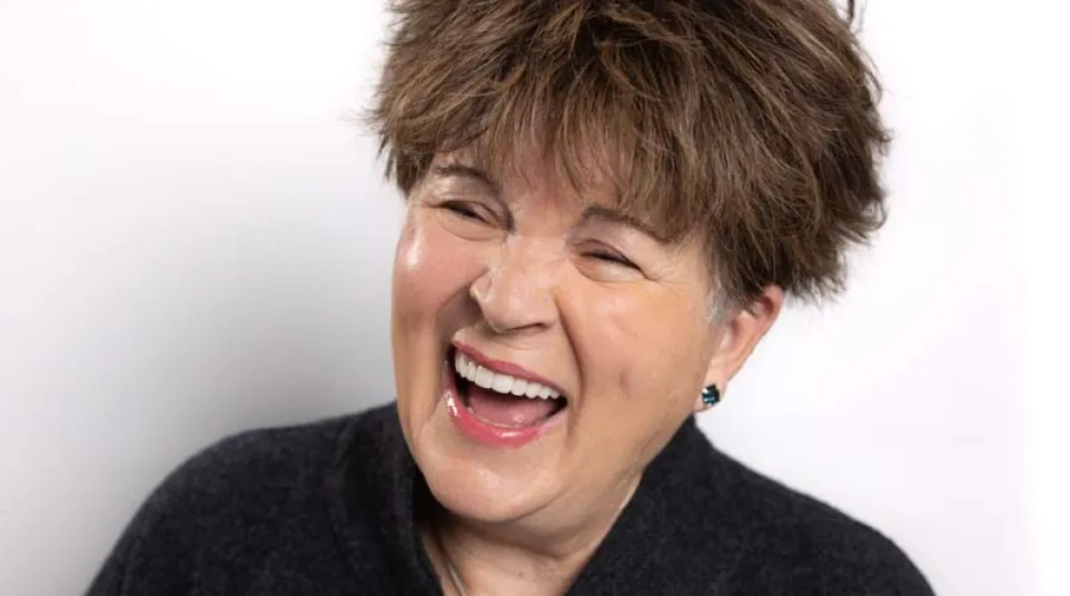 Middle-aged woman with short brown hair wearing black clothes laughing joyfully against white background