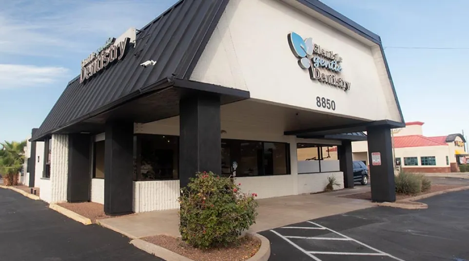 Exterior view of Glendale Gentle Dentistry building with black roof and parking area under a blue sky.