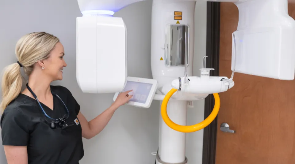 Dental professional operating a modern 3D panoramic X-ray machine in a clinic setting.