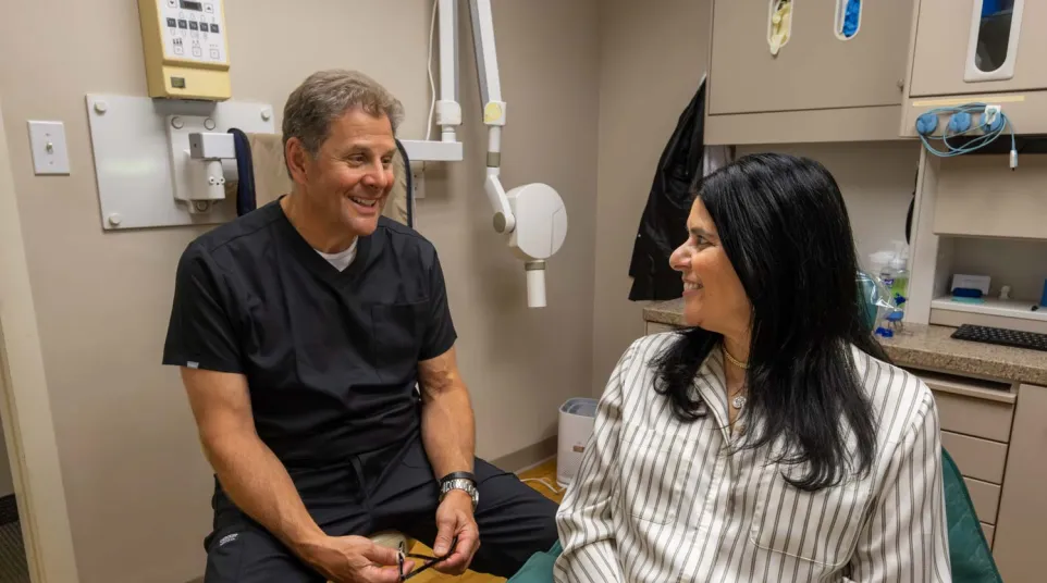 Dentist and patient smiling and discussing treatment in a modern dental office with equipment in background