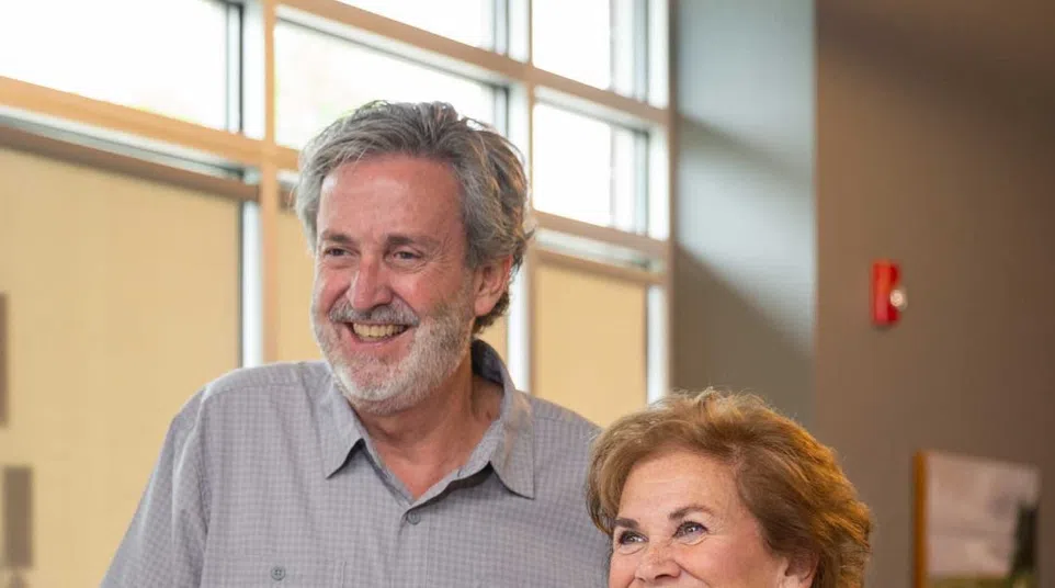 Smiling senior couple standing indoors near window, engaging happily in a bright modern room.