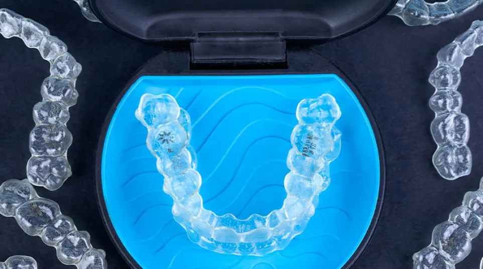 Clear dental aligners arranged around a blue and black case with one aligner inside the case.