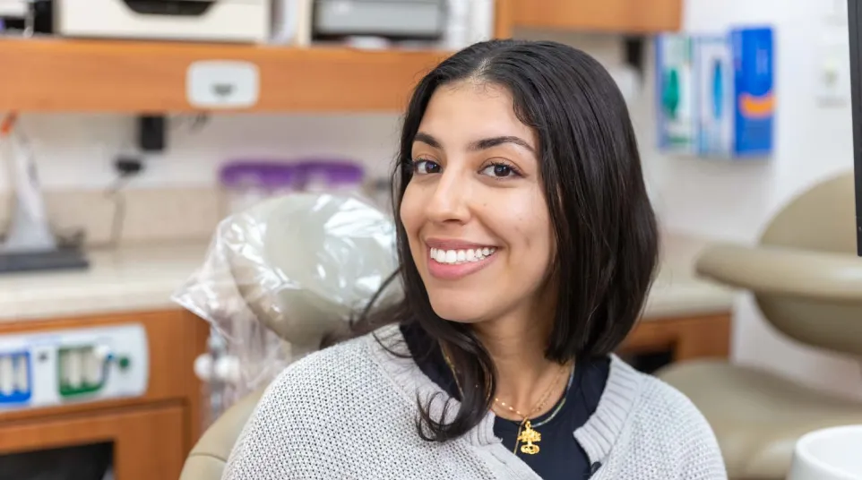 Smiling young woman sitting in a dental chair in a modern dental clinic setting looking at camera