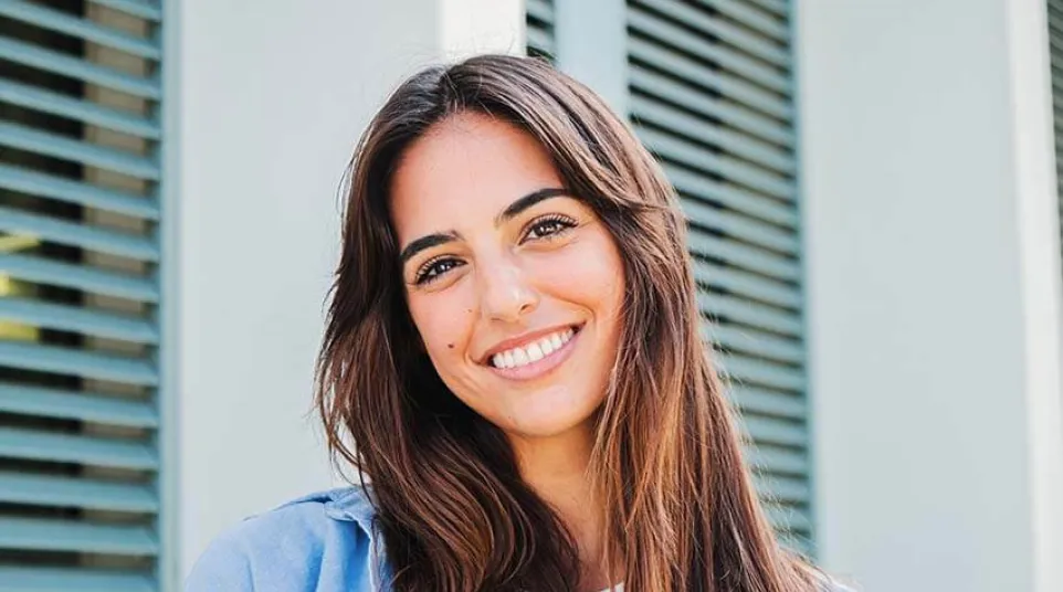 Smiling woman with long hair stands in front of a modern building with green shutters.