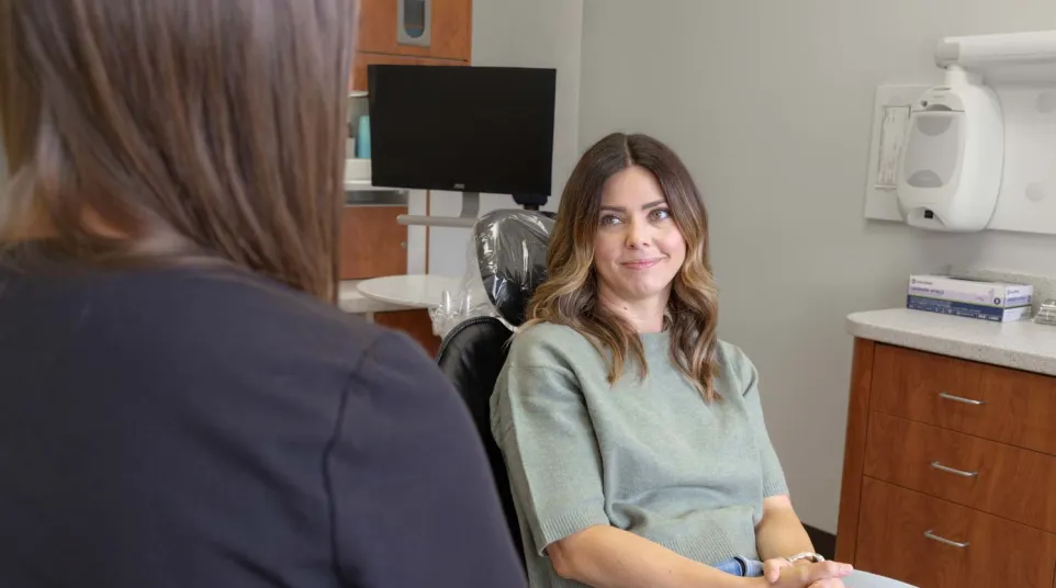 Woman sitting in dental chair smiling during consultation with dental hygienist in modern clinic.