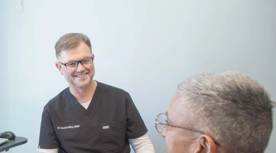 Dr. Scott Fitts in black scrubs smiles to a  patient