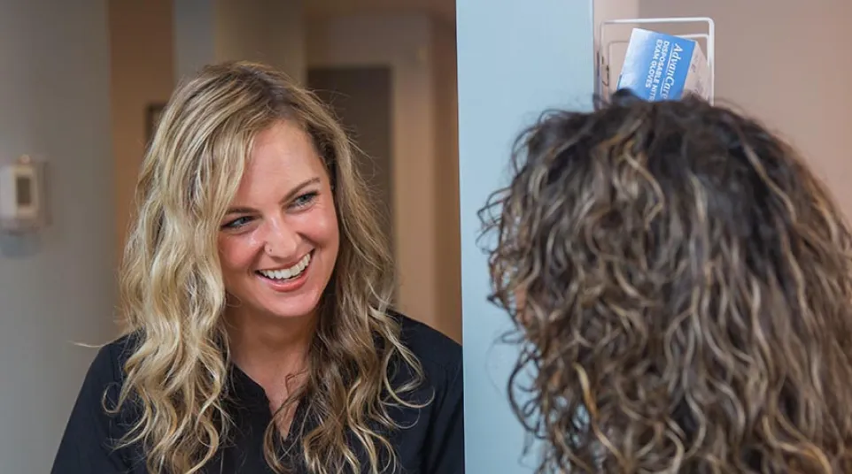 Two women in black scrubs review a yellow file folder while smiling and talking in a medical office.