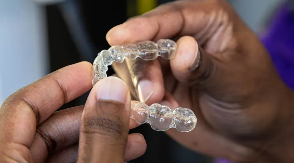 Close-up of hands holding a clear dental aligner for orthodontic teeth straightening treatment.