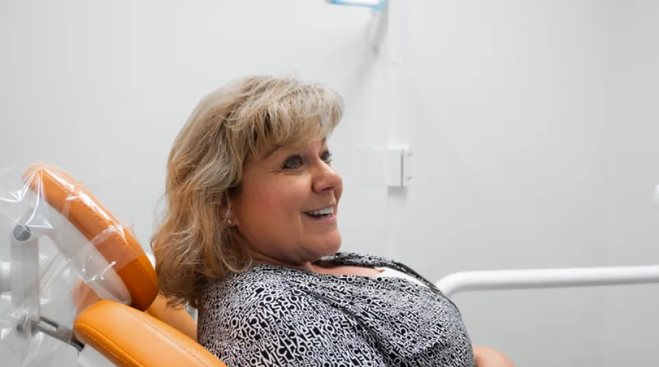 Middle-aged woman smiling while sitting in an orange dental chair inside a modern clinic room.