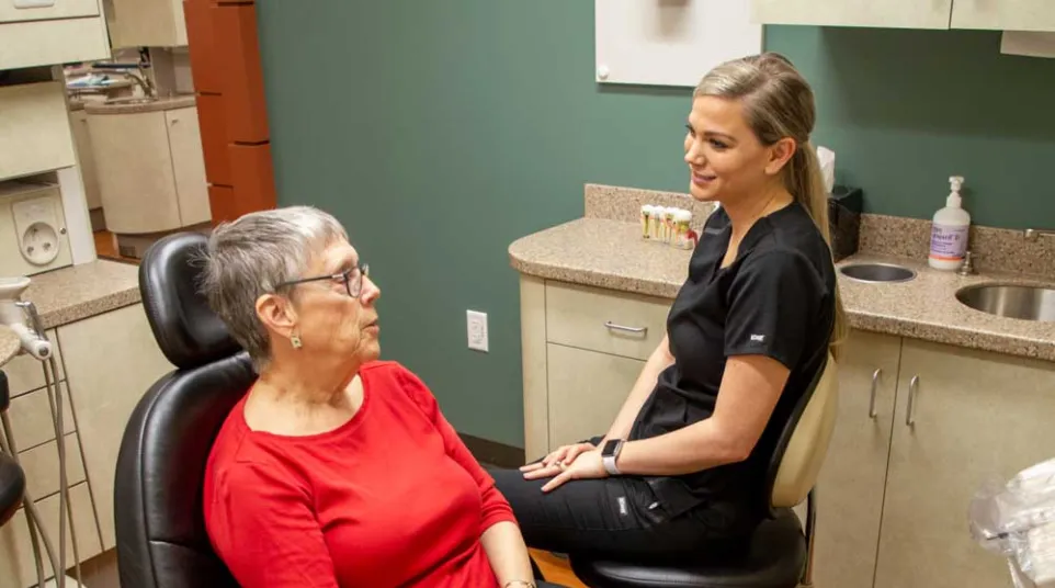 Senior woman in red shirt talking to female dental professional in clinic with modern equipment