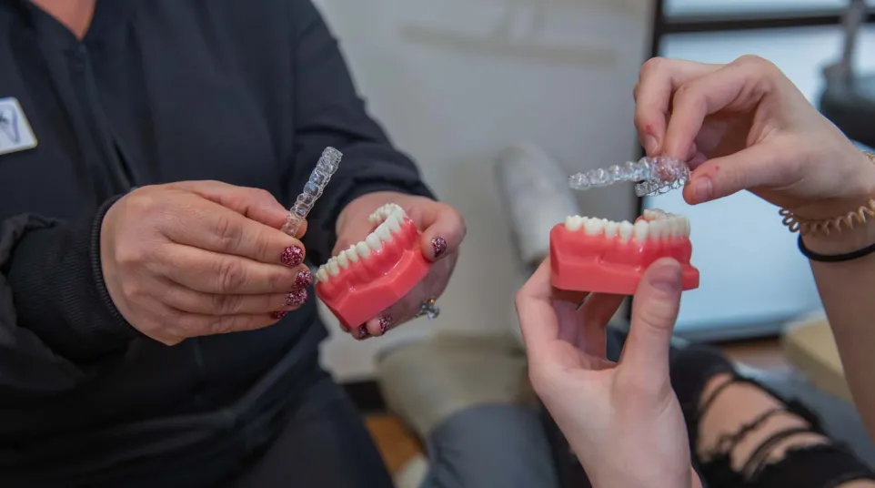 Two people holding dental molds and clear orthodontic aligners demonstrating teeth alignment.