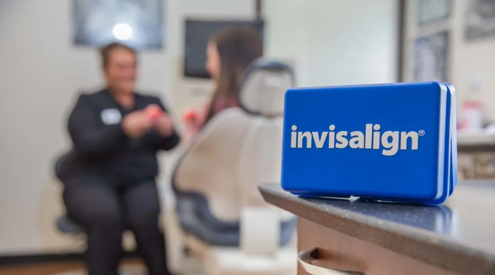 Blue Invisalign case on countertop in dental office with patient and dentist in blurred background.