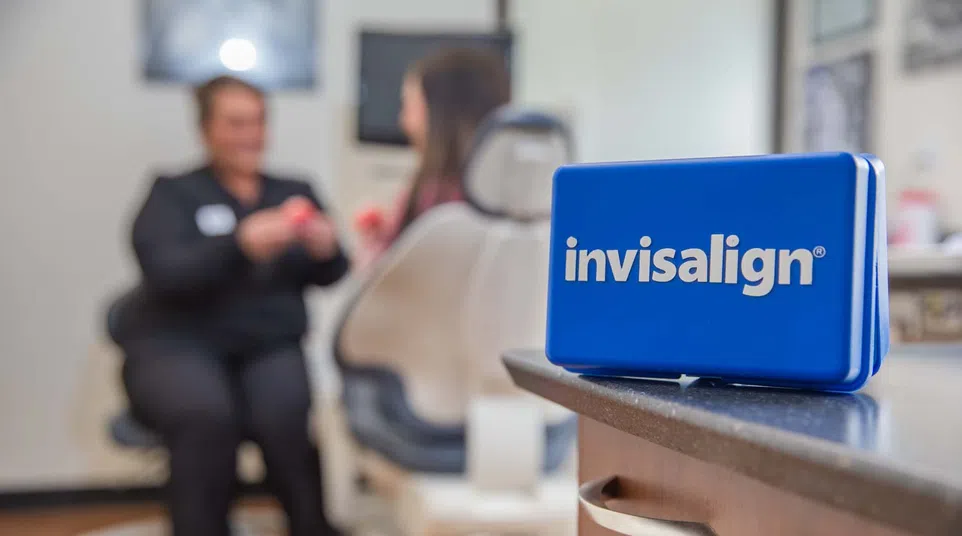 Blue Invisalign case on countertop in dental office with patient and dentist in blurred background.