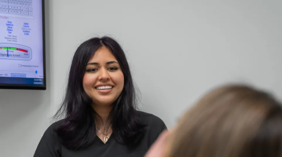 Smiling female healthcare professional talking to a patient in a clinical setting with medical monitor in background