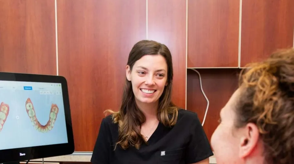 Dentist smiling and consulting with patient while dental 3D images display on computer screen in clinic.