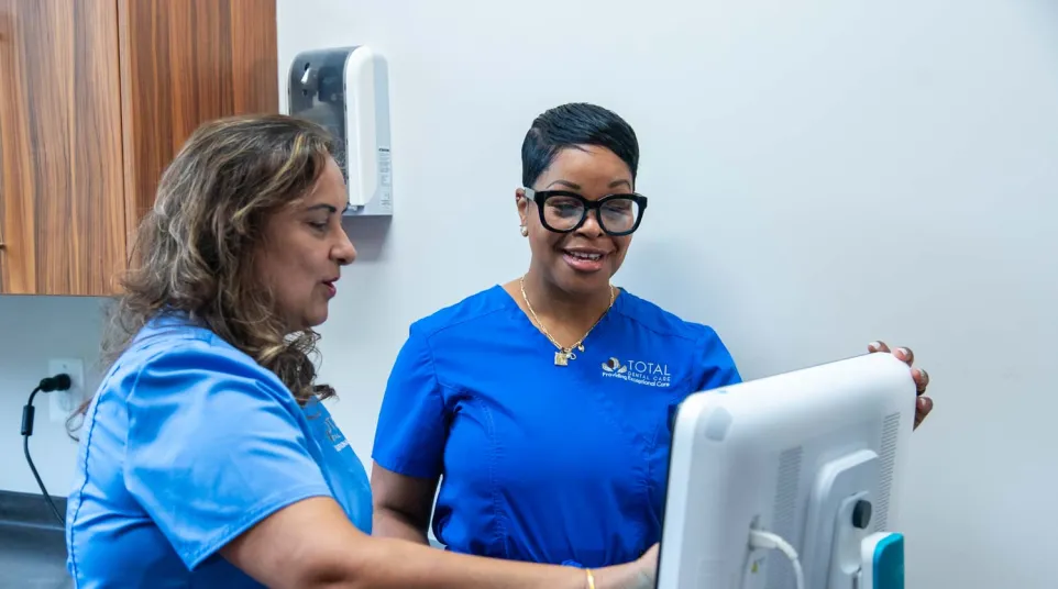 Two healthcare professionals in blue scrubs reviewing patient information on a computer in a clinical setting